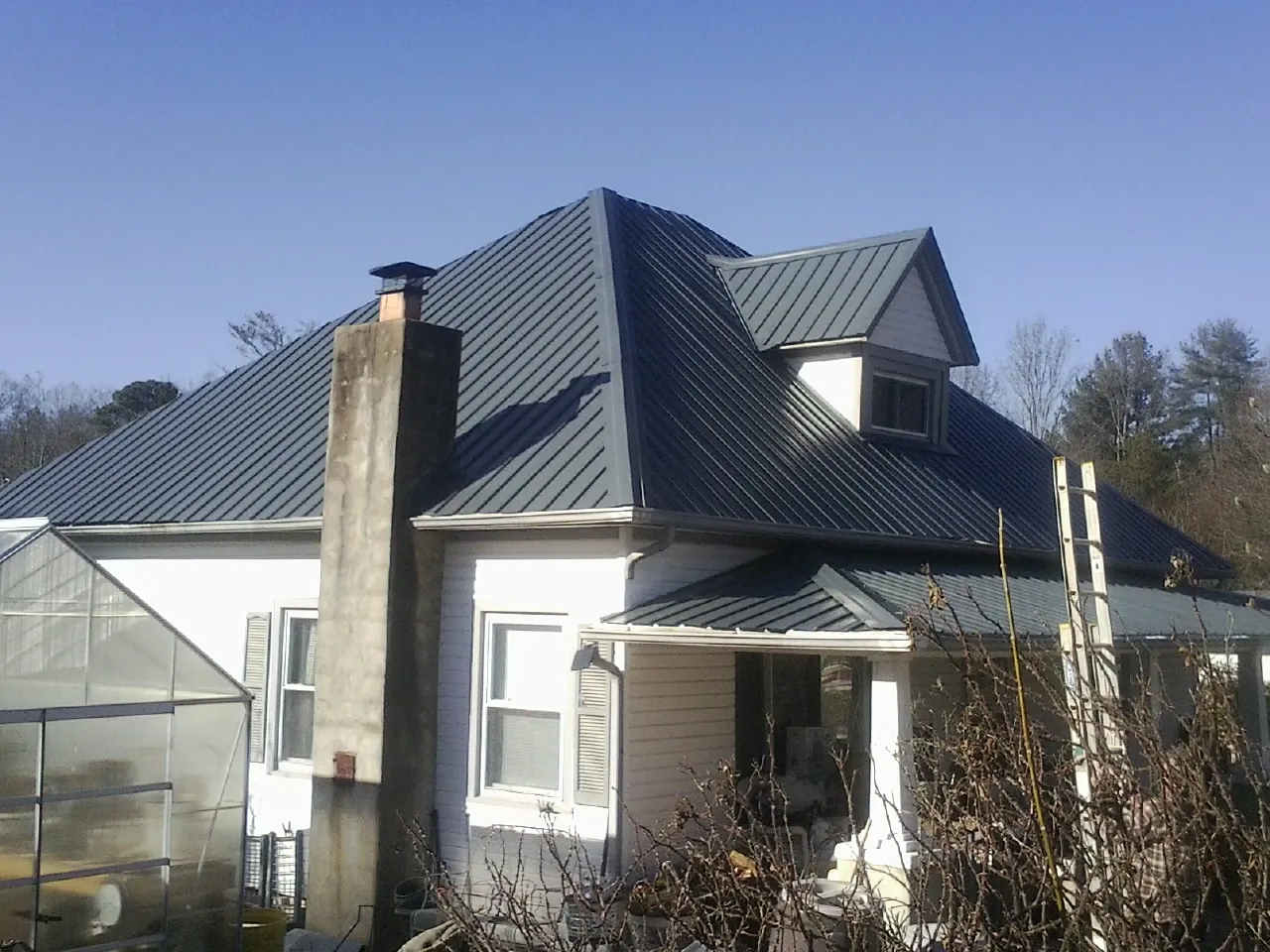 Dark blue standing seam metal roof on a white farmhouse with dormer — Slate & Tile Roof Repair by Roofing Brothers in Clay City