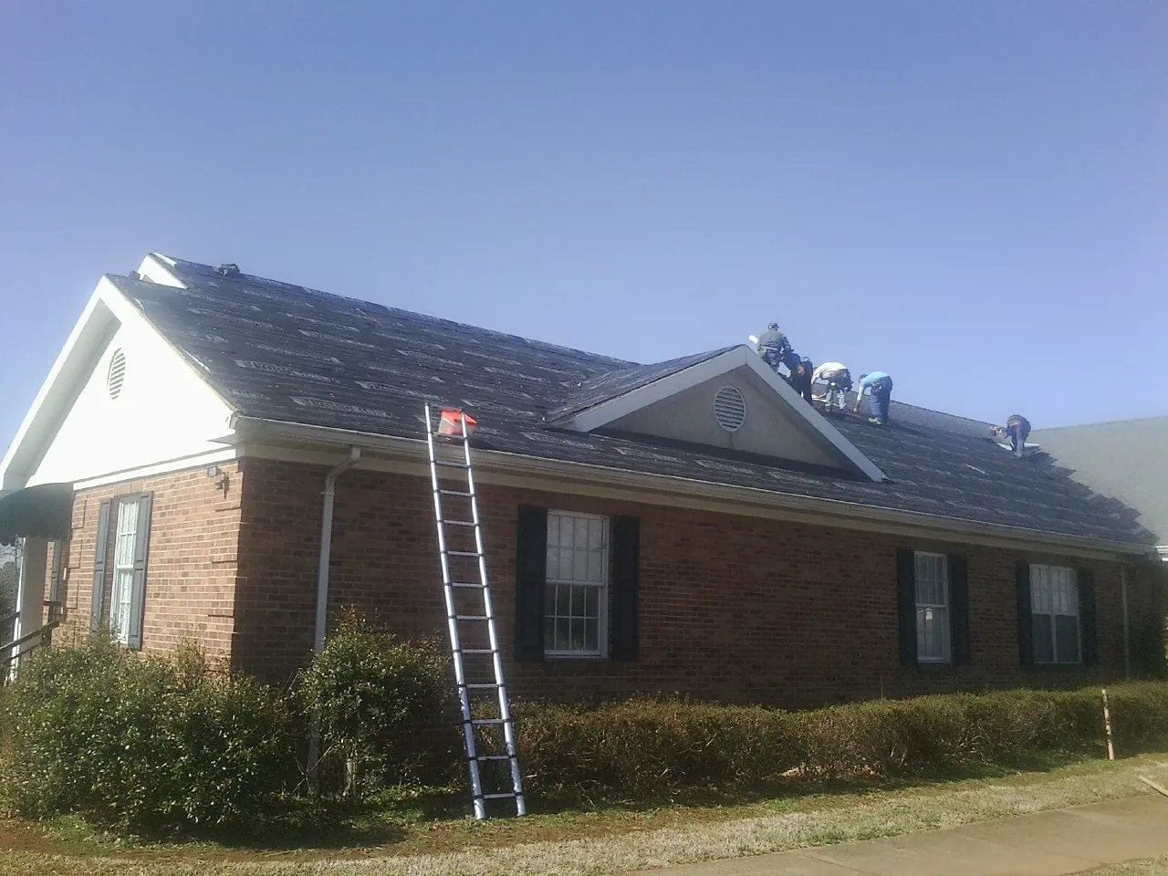 Crew tearing shingles off a brick ranch roof with a ladder set — Emergency Roof Repair work by our crew in Clay City