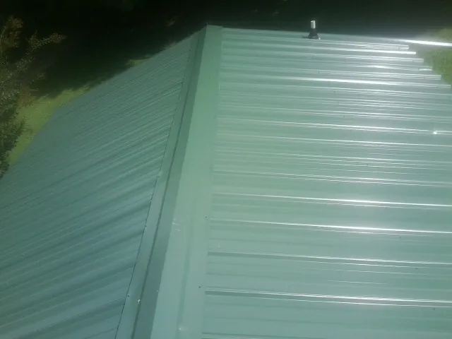 New green metal panels meeting at the ridge of a roof — Flat Roof Repair work by our crew in Clay City