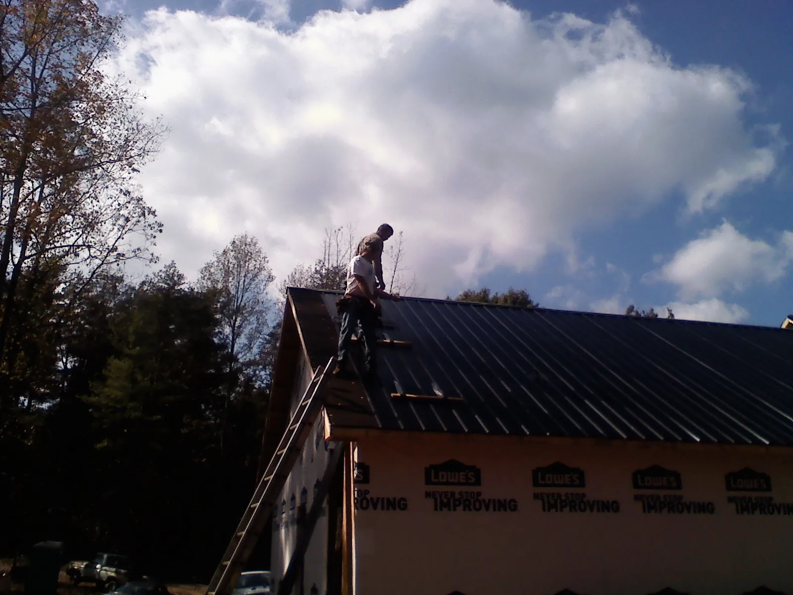 Roofer fastening dark metal panels high against a cloudy sky, from a Roof Inspection job in Clay City
