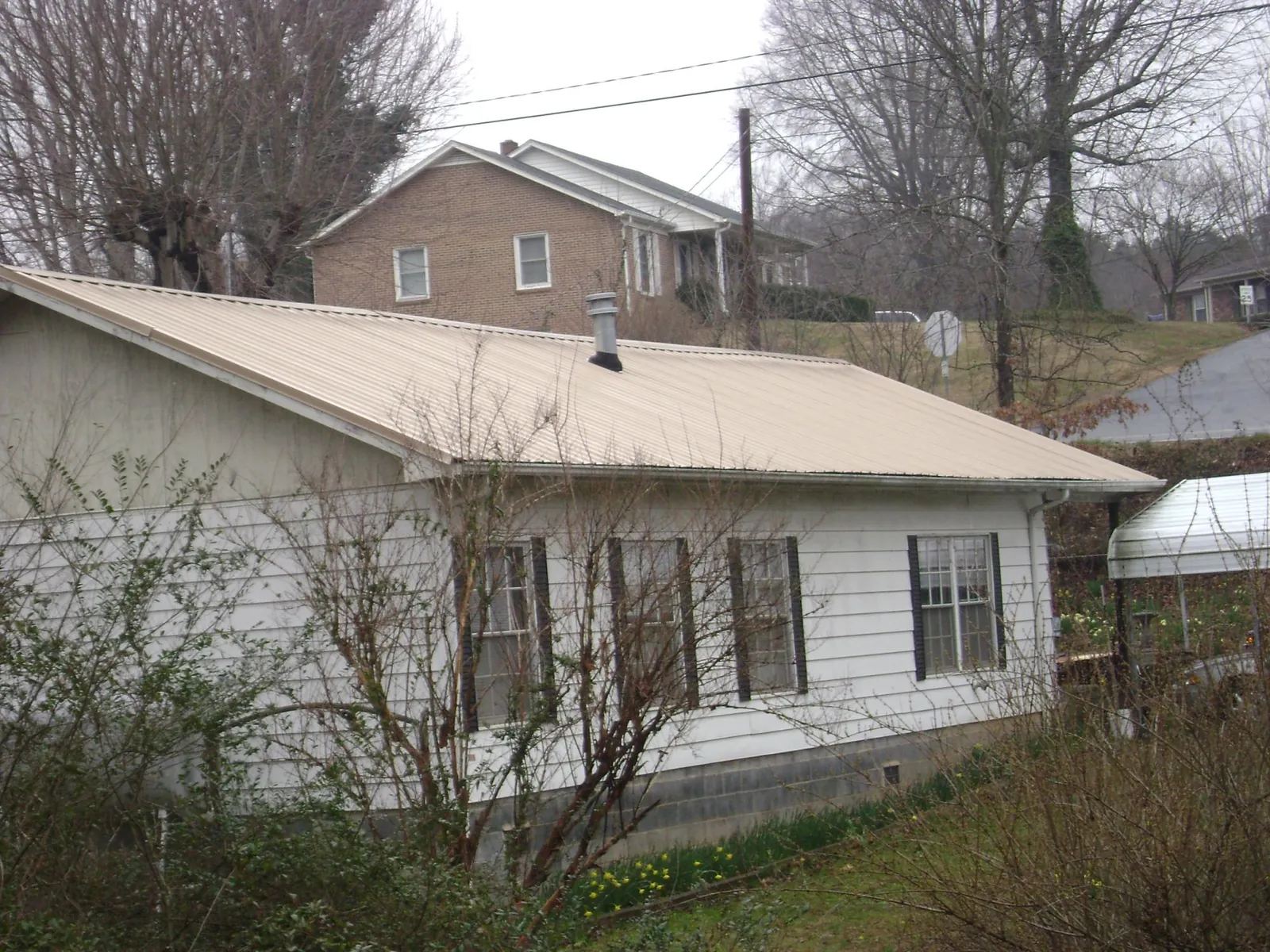 Tan metal roof on a white sided house set into a hillside — Commercial Roofing by Roofing Brothers in Clay City